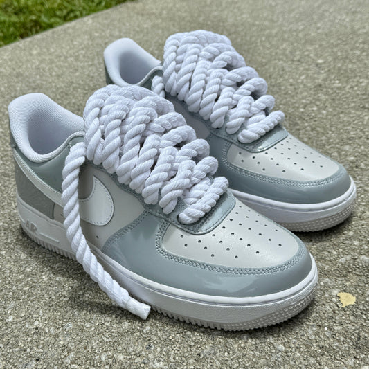 Gray and white air force one sneakers with white rope laces on a concrete surface