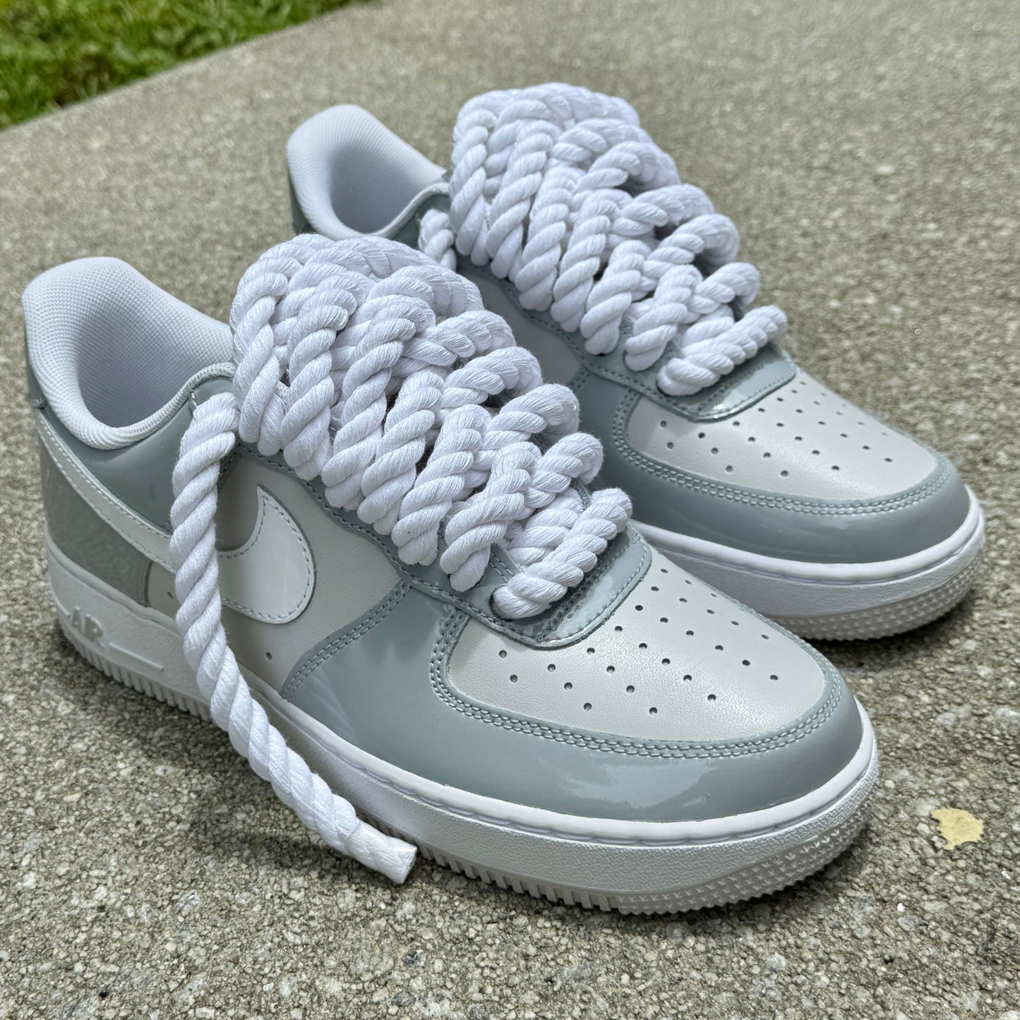 Gray and white air force one sneakers with white rope laces on a concrete surface