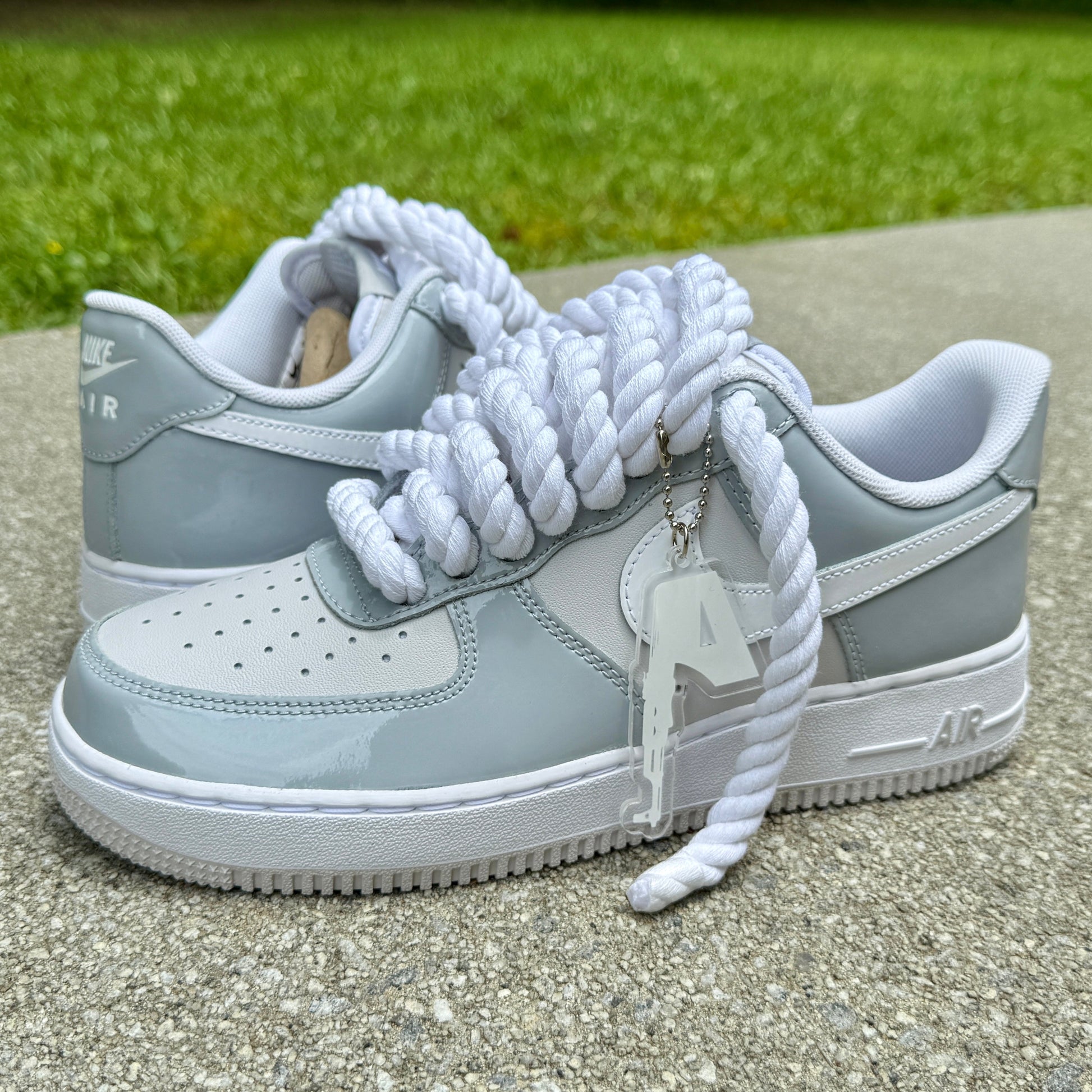 Gray af1 sneakers with white laces and a keychain on a concrete surface with grass in the background